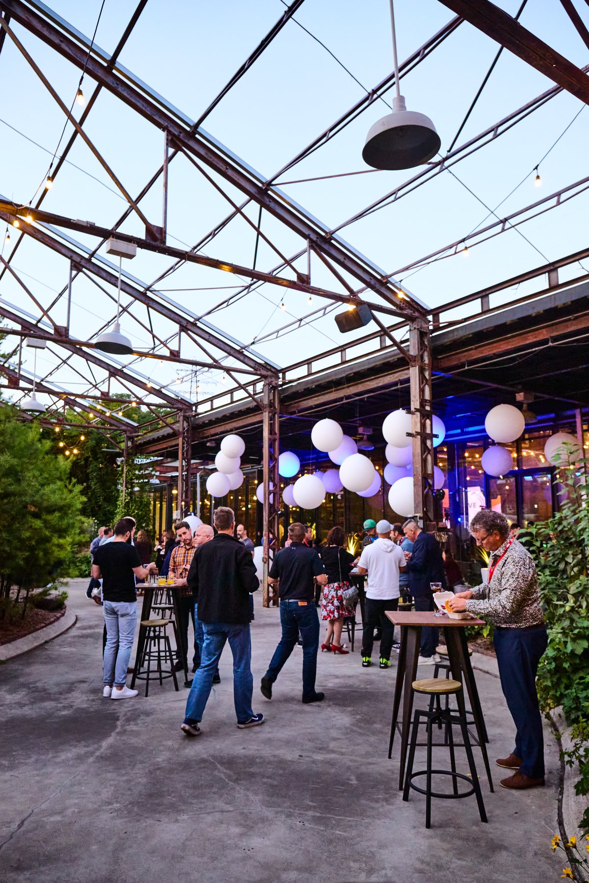 Guests mingling at cocktail tables under string lights at dusk